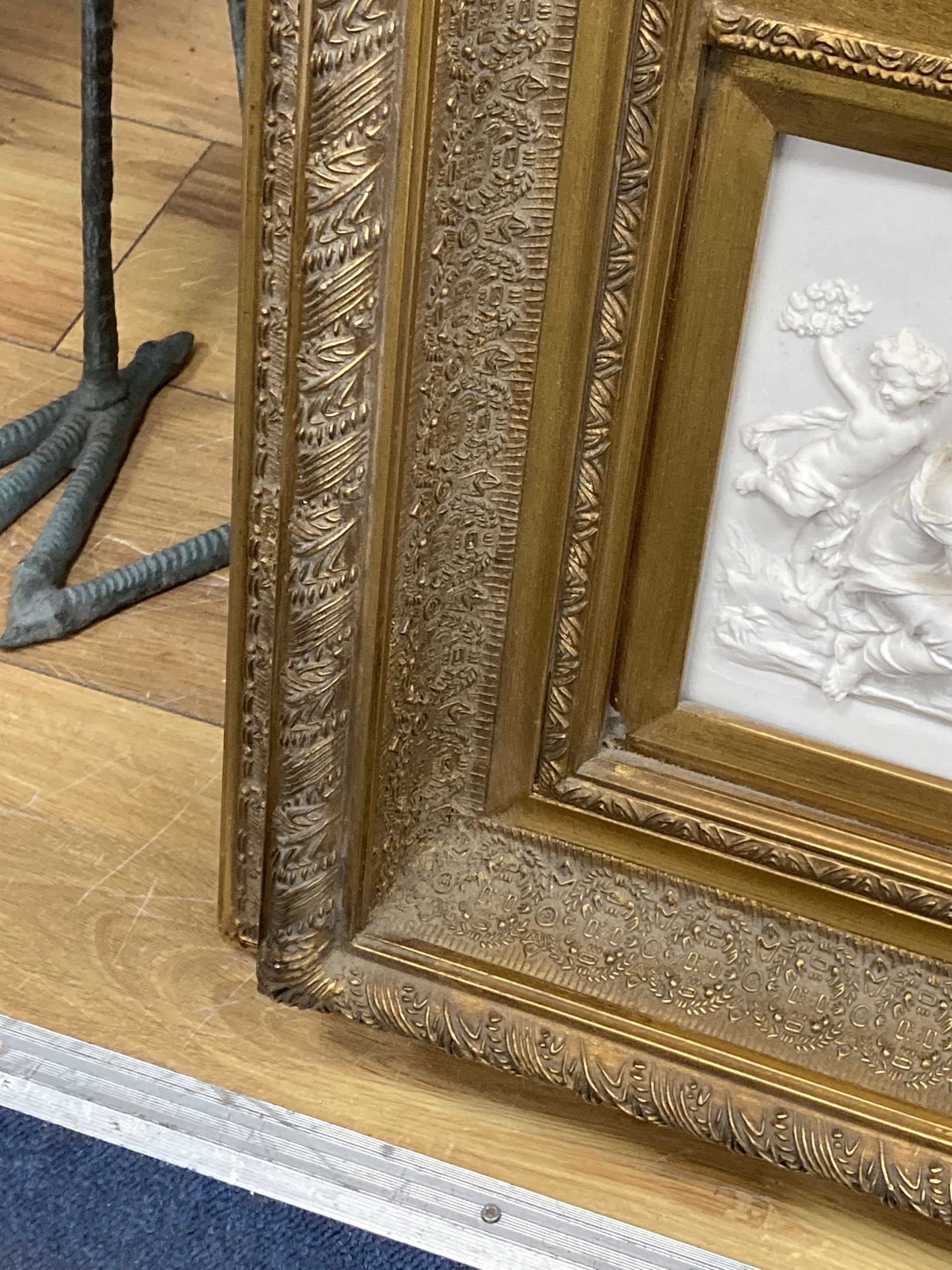 A gilt framed mirror, the base inset with a composition relief depicting putti at play, width 56cm, height 105cm